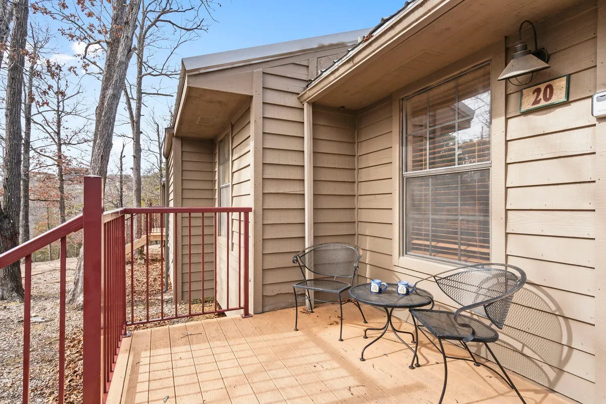 A cozy private porch with two metal chairs and a small table set on a wooden deck with a distinctive red railing. Surrounded by lush greenery, the porch offers an intimate space to relax and enjoy the outdoors, with hints of wildlife and tranquil sunrise views.