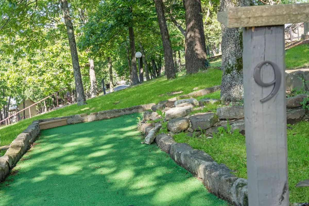 A cheerful mini-golf course with a bright green putting surface, framed by natural stone borders and playful signage. The area is surrounded by lush greenery, creating a welcoming environment for family outings and friendly competition.