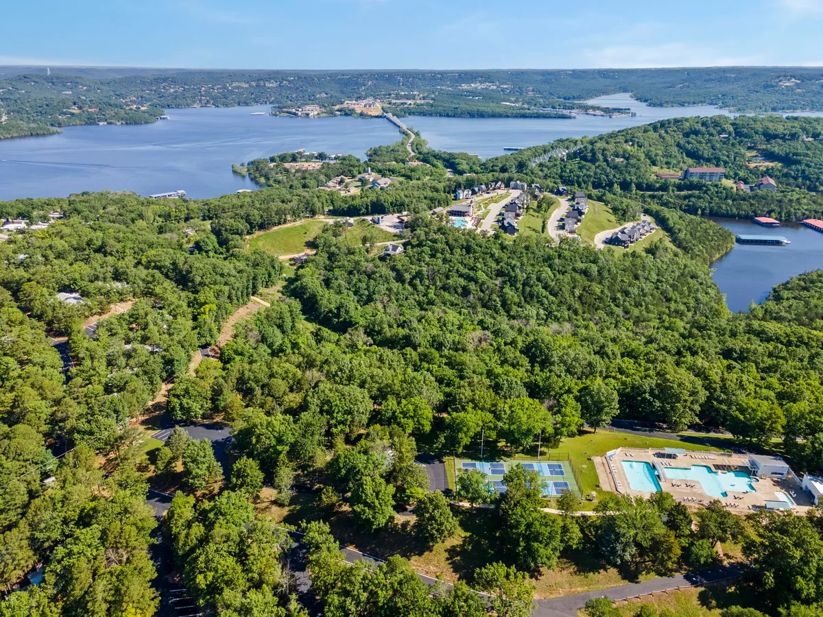 A panoramic exterior shot featuring multiple resort amenities: sparkling lakes, swimming pools, tennis courts, and lush residential areas, all surrounded by greenery. The image captures the vibrancy of the resort community and the close-knit relationship between recreation, water activities, and relaxation.