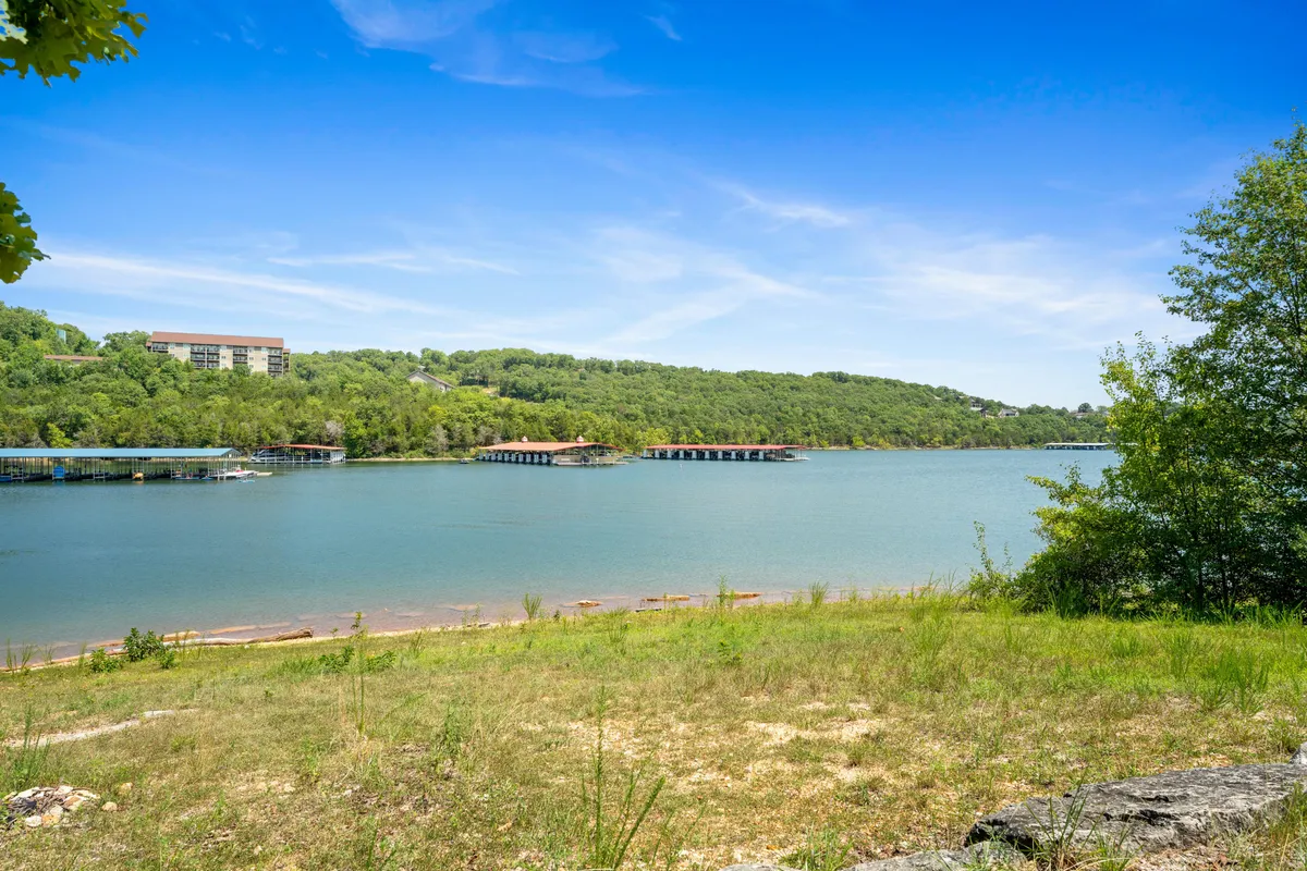 A tranquil view of a calm lake bordered by green hills with docks extending into the water and a clear blue sky above. The setting is ideal for fishing, boating, and relaxing by the lake, evoking a sense of peace and possibility for adventure or unwinding.