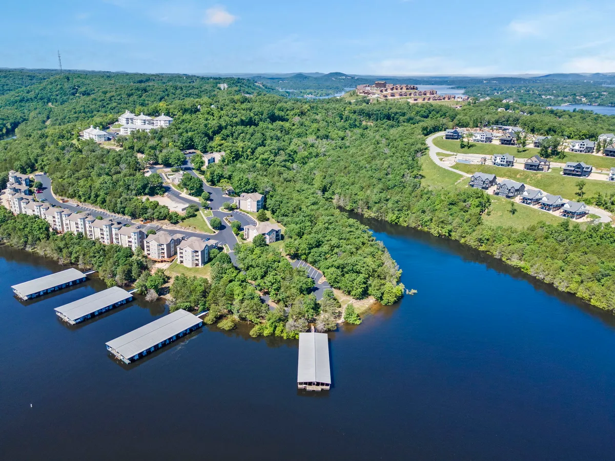 A wide exterior view of the lake edged by marinas with boats, lush greenery, and hillside homes in the distance. The image captures a golden hour glow, suggesting the transition between day and romantic evening. Scenic walking areas line the water, and the peacefulness of the lake is emphasized by still water and open skies.
