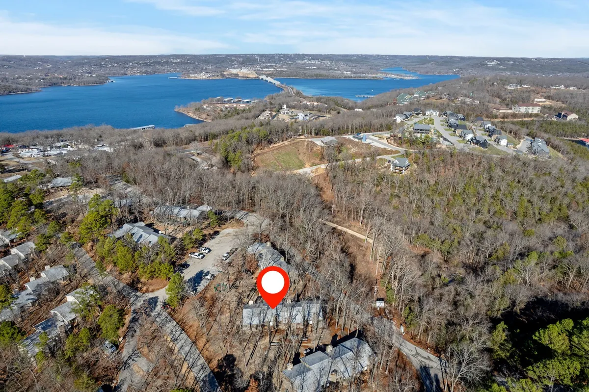 A sweeping vantage point of the lake bordered by dense forest, with residential buildings dotted along the shore. The scene evokes a sense of retreat, with nature trails winding through the woods and the shimmering water inviting exploration or quiet observation.