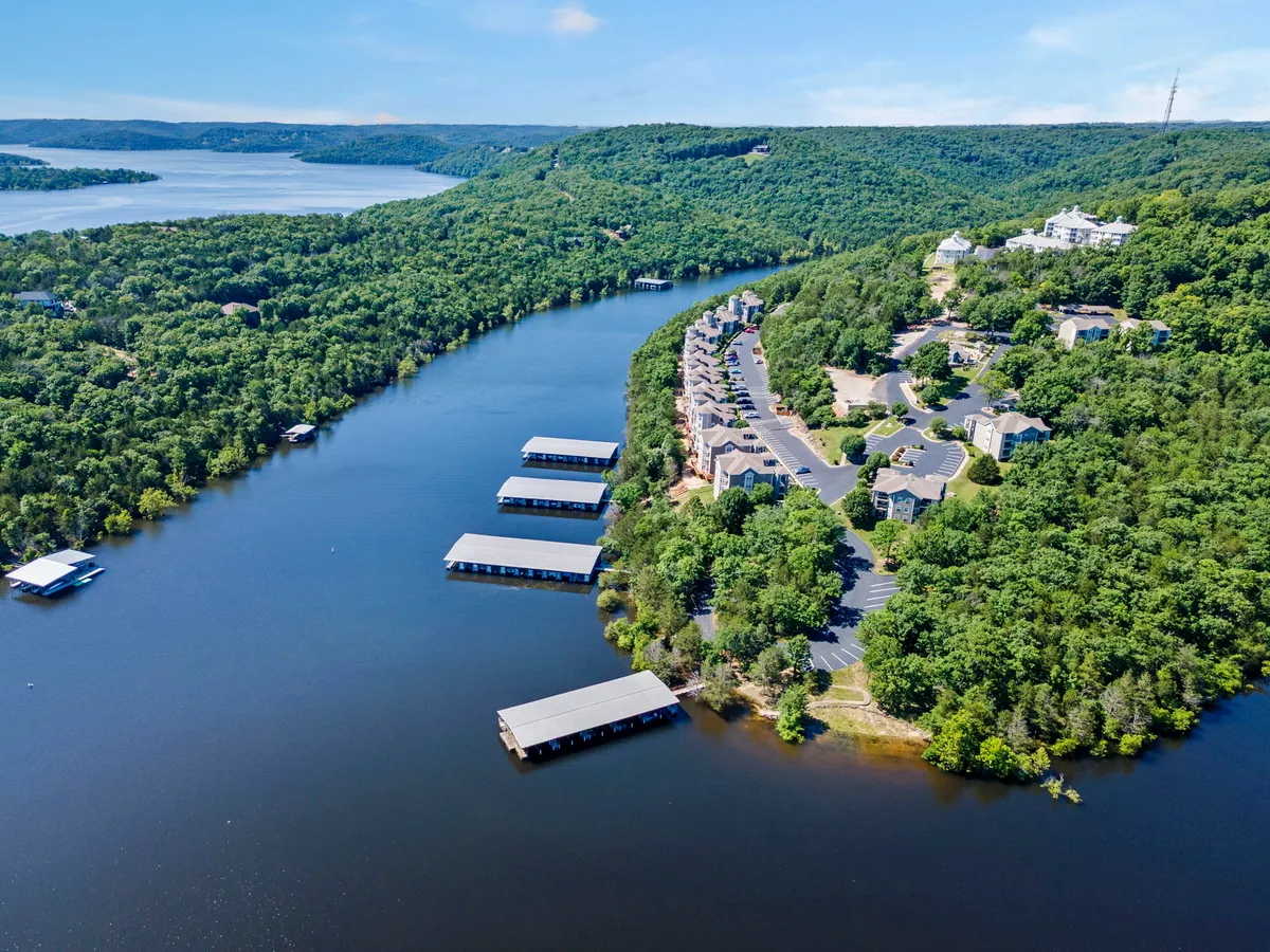 Serene riverfront with boathouses and residential areas surrounded by greenery. The image evokes relaxation, with options for boating, hiking nearby trails, and taking in sunset views over the water, emphasizing the immersive outdoor experience available to guests.