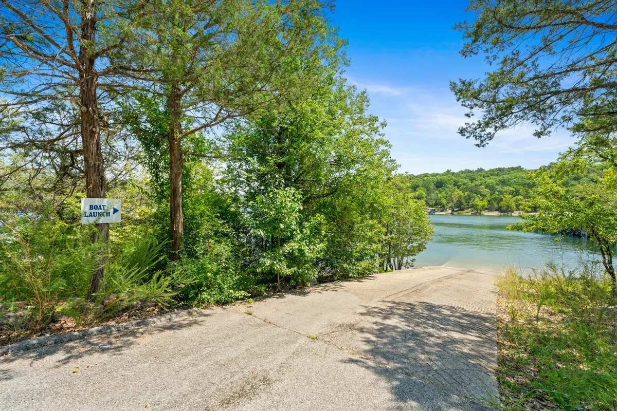 A lakeside boat launch area framed by lush greenery, with clear water just a few steps away and a sign marking the launch. The shoreline is natural and inviting, perfect for directly accessing the lake by boat, kayak, or for fishing right at the water's edge.