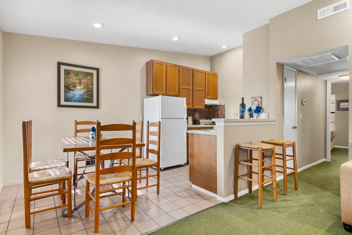 A cozy dining area with a wooden table set for a meal, adjacent to a fully equipped kitchen with visible appliances and framed artwork. The atmosphere invites shared meals and conversation, emphasizing togetherness and comfort.