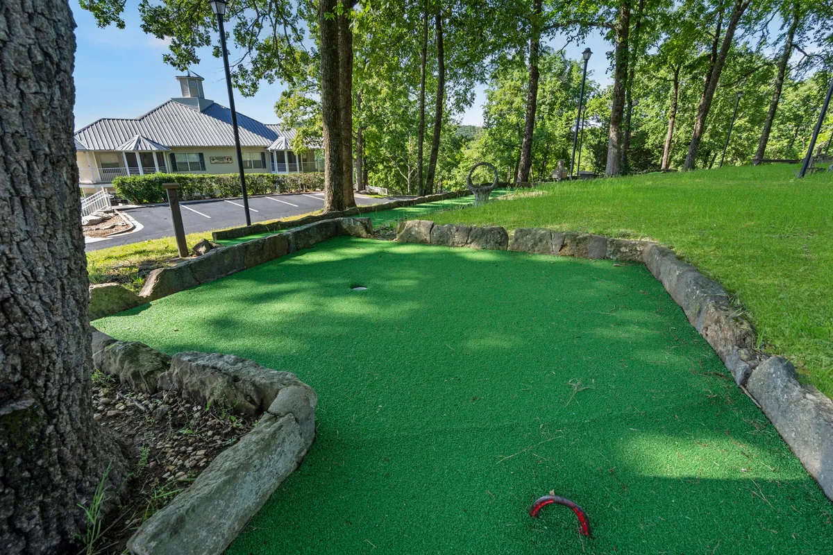 A playful mini-golf area set amid green artificial turf and surrounded by trees, with a scenic backdrop. The atmosphere is lively and inviting, suggesting family gatherings and friendly outdoor games.