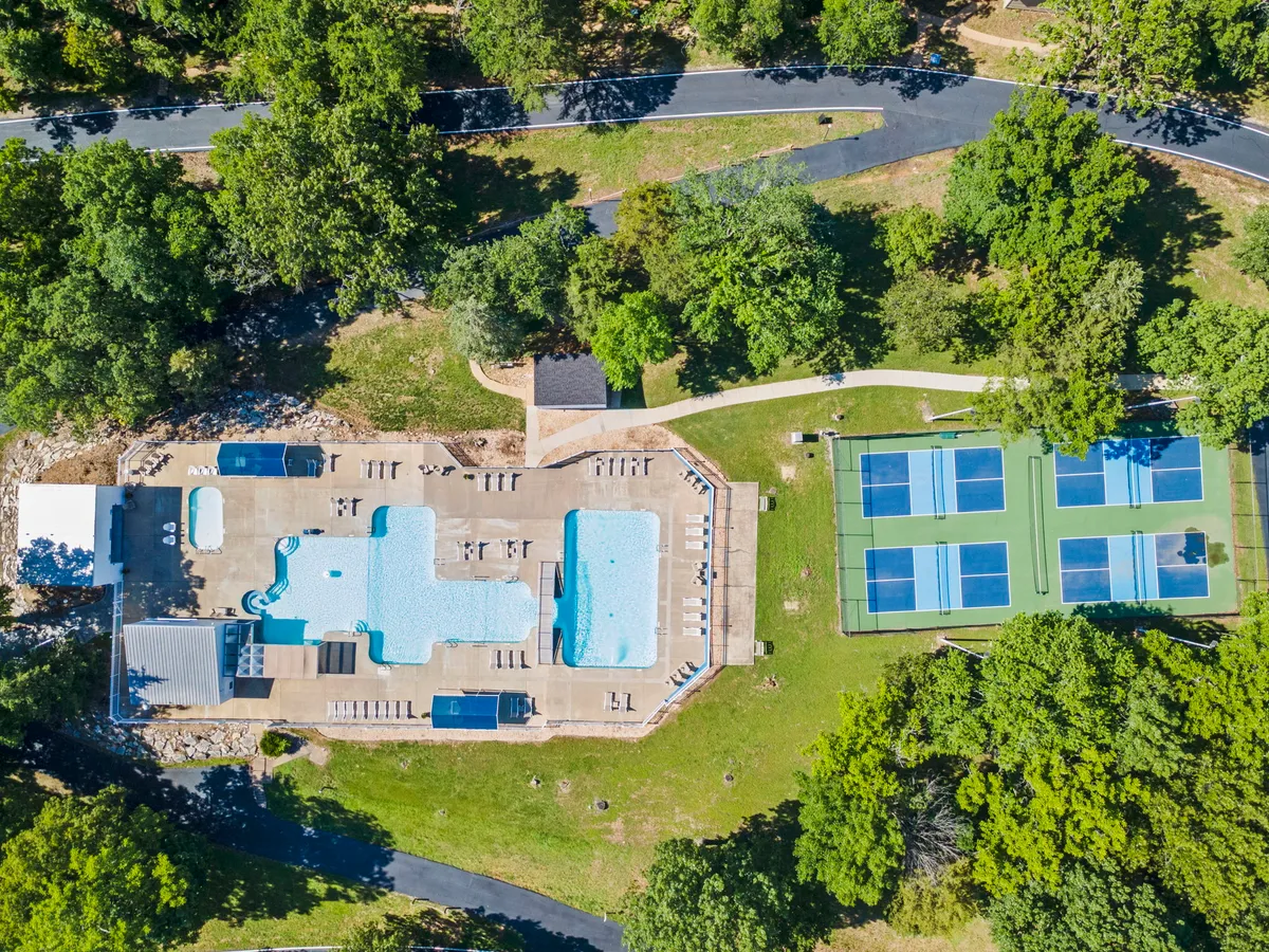 A lively outdoor recreation area featuring a sparkling swimming pool surrounded by lounge chairs and vibrant greenery. Adjacent to the pool, tennis courts invite energetic play, while the overall scene captures a sense of social activity and relaxation, ideal for group gatherings or family fun.