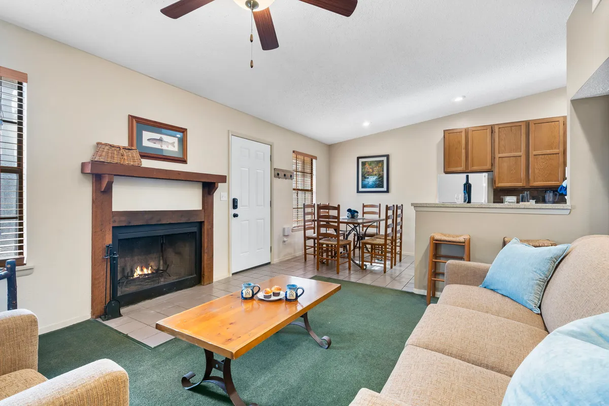 A warm, open living space featuring a glowing fireplace, a central coffee table, and a view into the adjoining dining area. The ambiance is cozy, with soft lighting and inviting furnishings that emphasize comfort and togetherness.