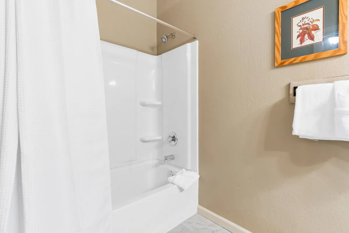 A clean, tranquil bathroom with a white shower curtain, towels neatly hanging on a rack, and framed artwork on the wall. The ambiance is fresh and inviting, hinting at a rejuvenating shower experience after an active day.