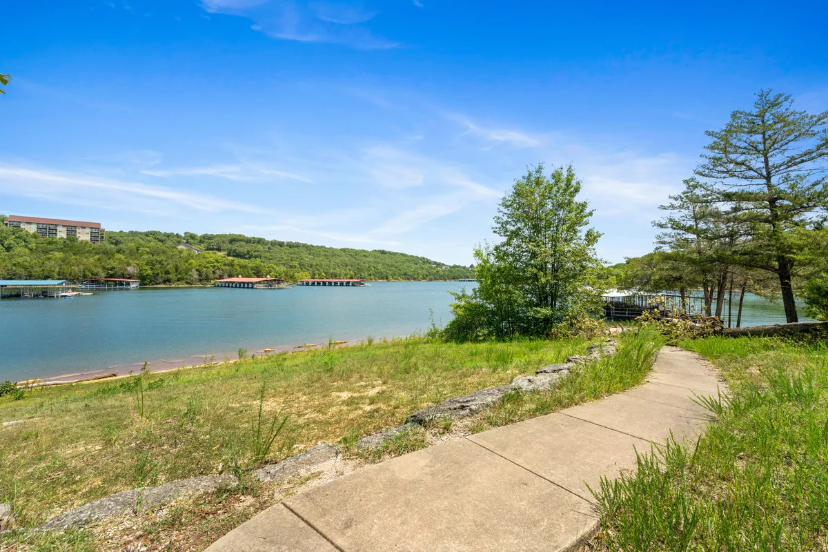 A tranquil pathway meanders along a riverside, bordered by trees and distant hills. The soft ambiance of sunset creates a peaceful setting ideal for walking or relaxing with a pet.