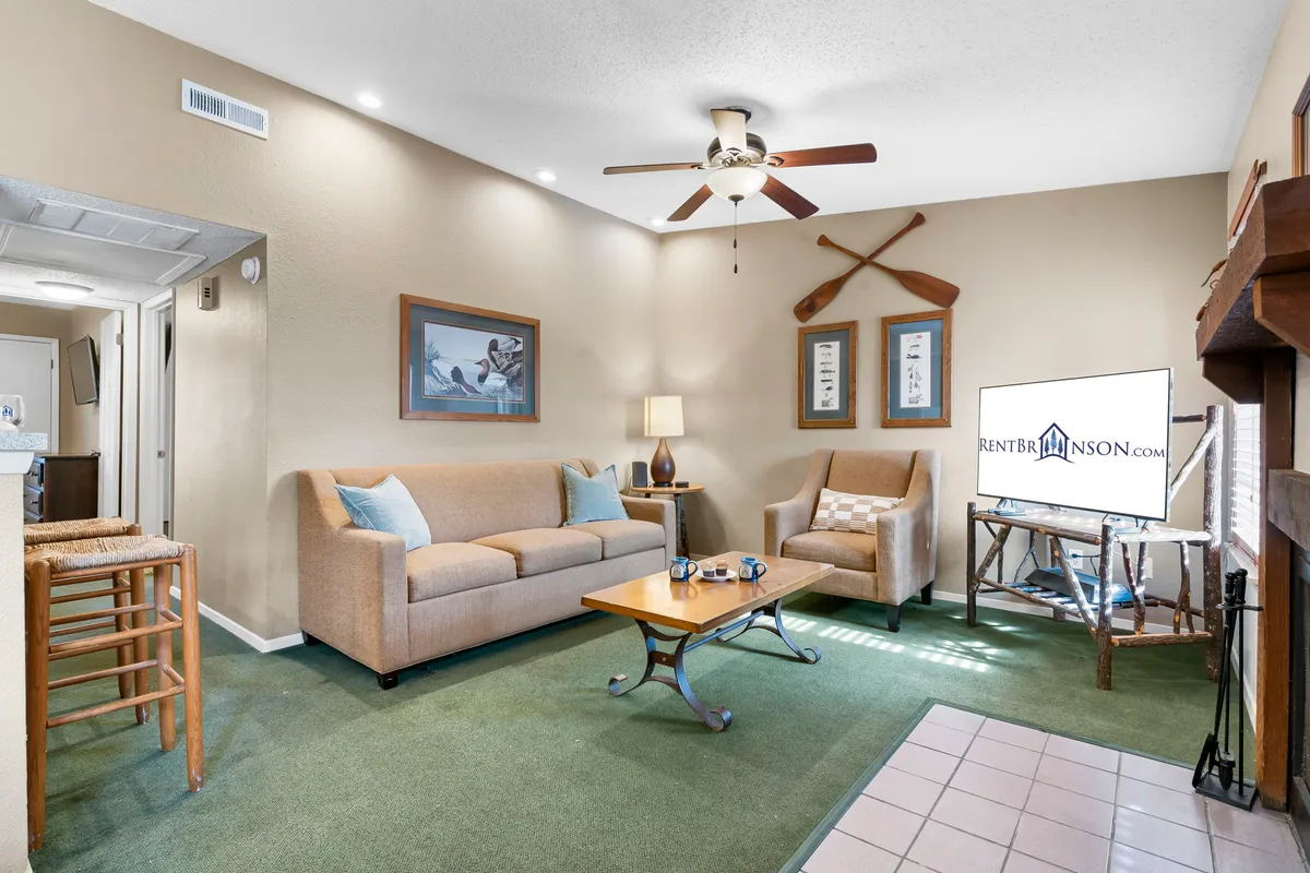 A cozy living room scene featuring a comfortable sofa, a coffee table, a lamp, a wall-mounted TV, and decorative oars on the wall. The arrangement invites relaxation and socializing, with seating oriented toward both entertainment and conversation.