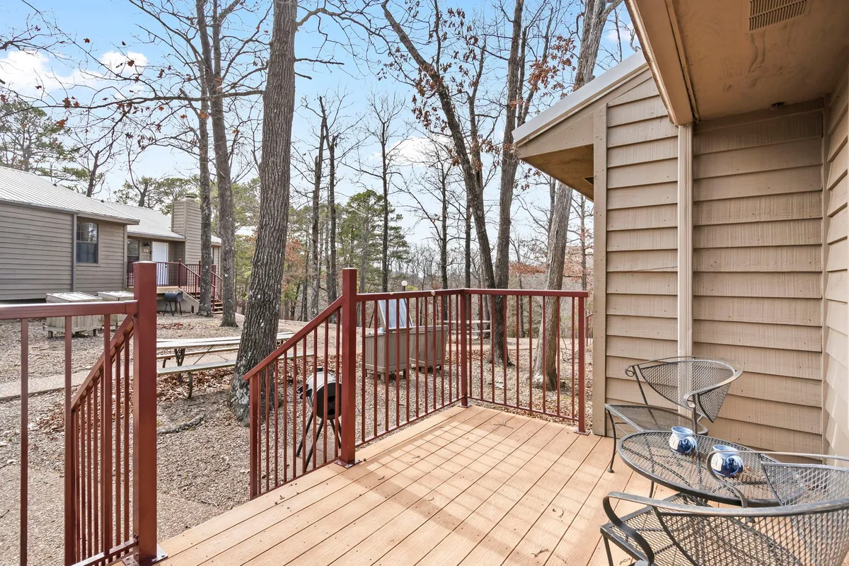 An exterior shot of a private deck with outdoor chairs and a decorative table, surrounded by trees. The scene invites relaxation, with dappled sunlight and a view into the wooded surroundings.