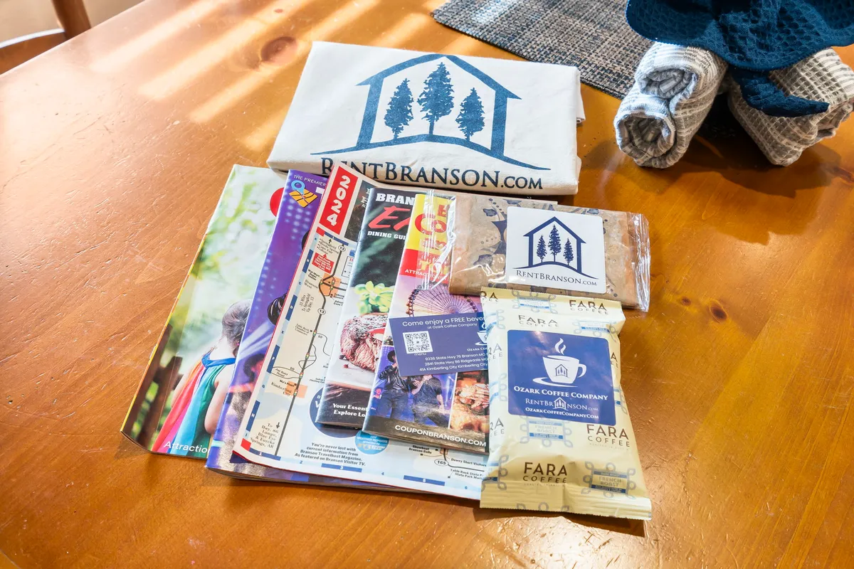 A cozy interior scene featuring a kitchen table laid out with brochures for local attractions, coffee packets, and a t-shirt, creating an inviting atmosphere for guests planning their Ozarks adventures while enjoying a cup of coffee. The mix of local information and relaxed hospitality is evident.