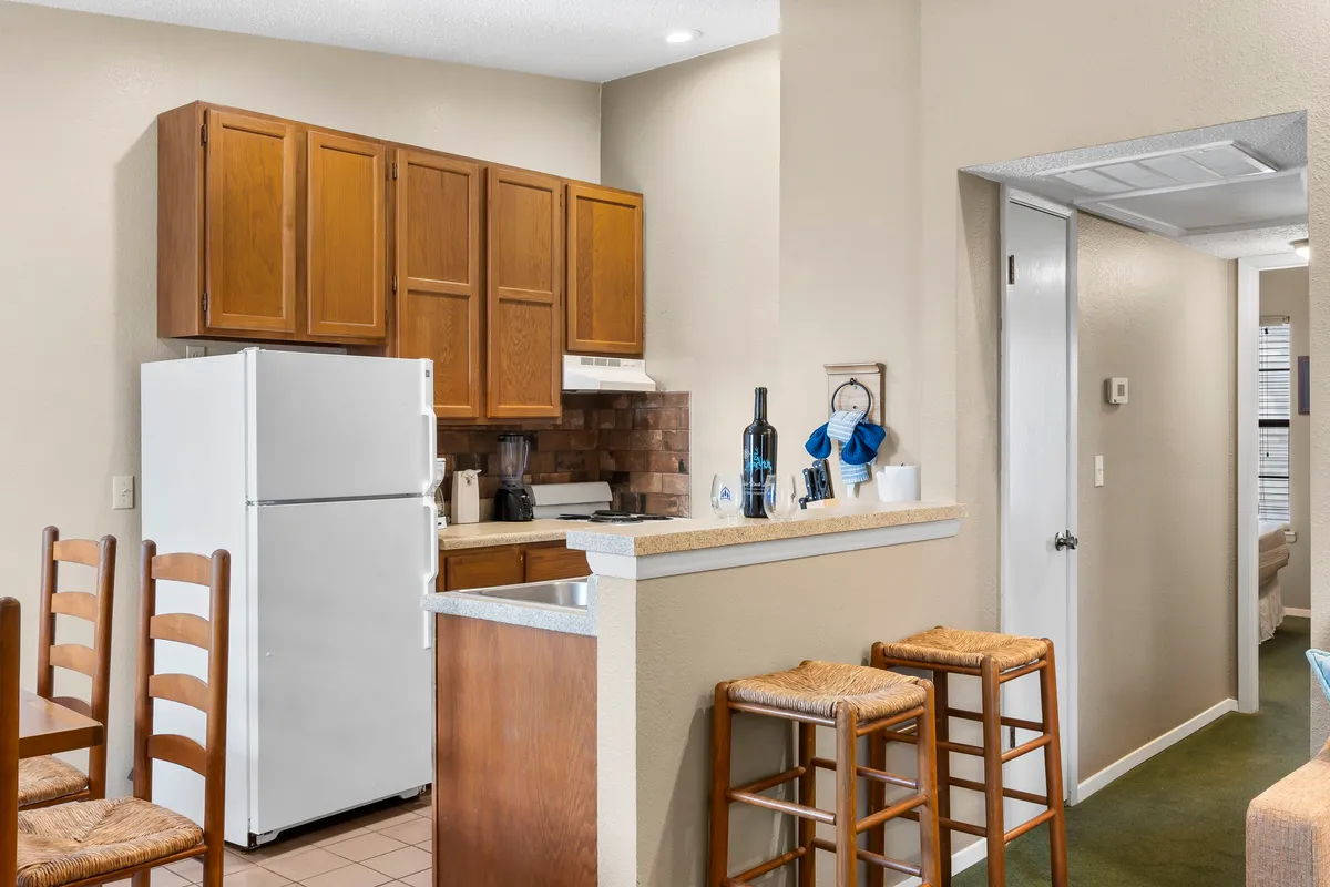 A modern kitchen featuring sleek cabinetry, an accessible countertop with bar stools, and a stainless steel refrigerator. The space is bright and open, perfect for meal prep or casual breakfasts.